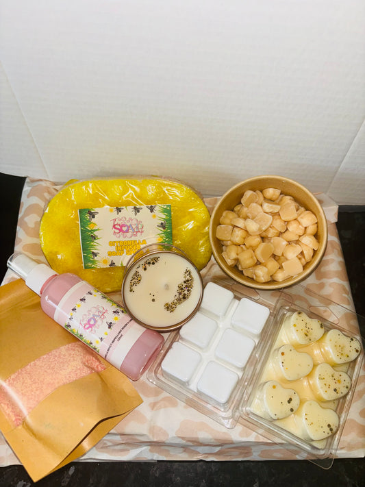 A collection of skincare products including a yellow soap bar, bath salts, lotion, wax melts, and heart-shaped bath melts arranged on a surface. Discover the ultimate surprise with our Mystery Box from The Soap Gal x, enhancing both your home fragrance and self-care routine.